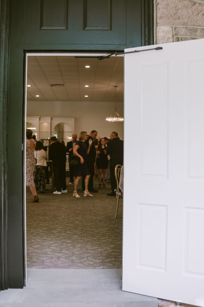 People gathered and talking inside a well-lit room, seen through a partially open door.
