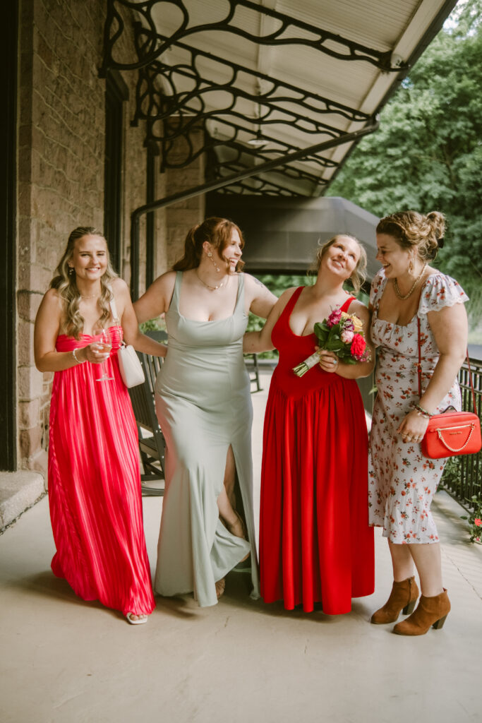 Four women in colorful dresses smiling and walking together on a covered outdoor walkway.