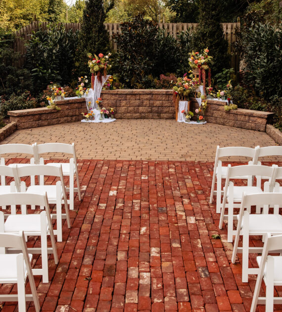 Outdoor wedding ceremony setup with white chairs facing a floral-decorated altar on a brick walkway.