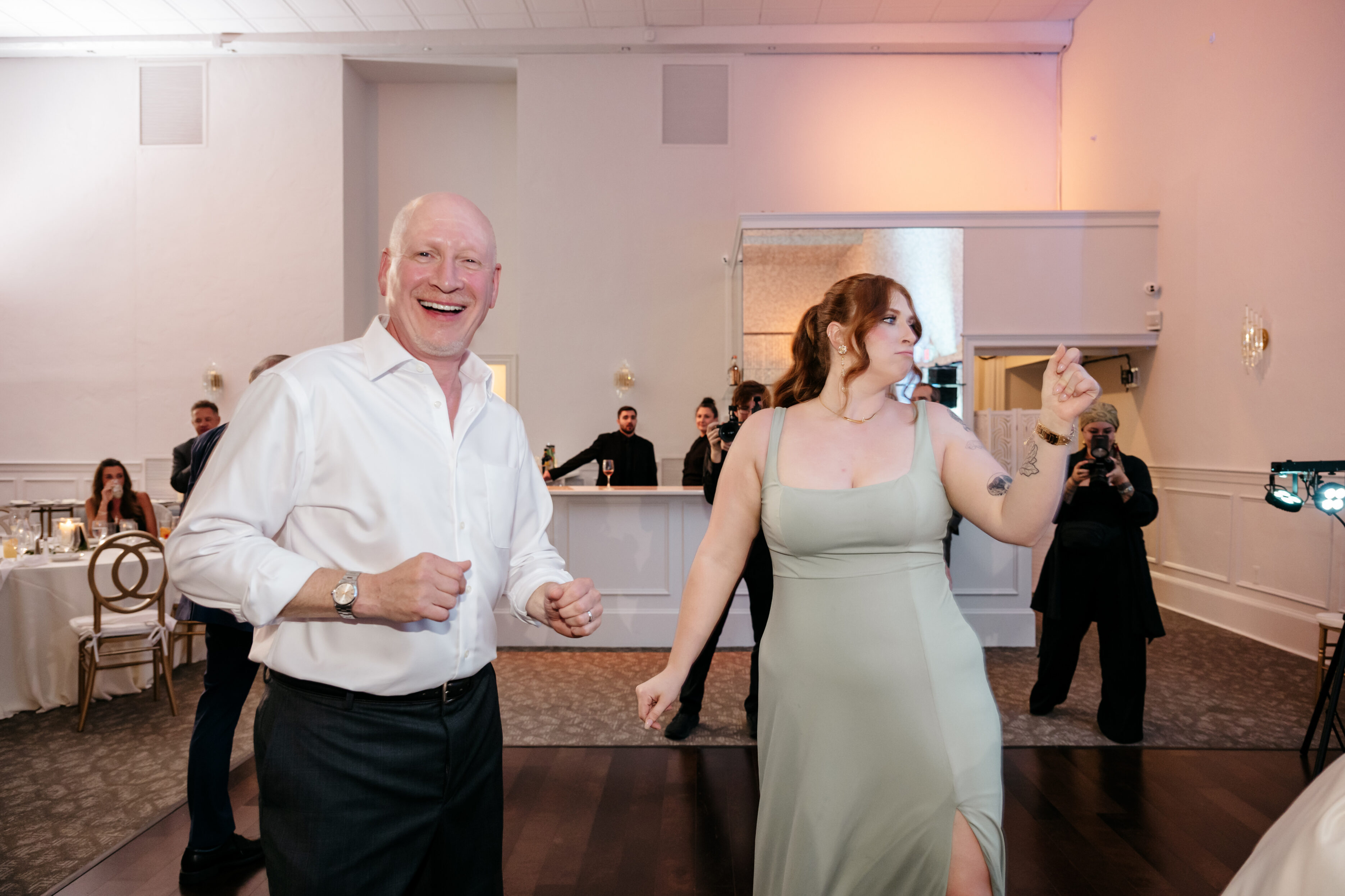 A smiling man and a woman in a green dress dance together at a formal indoor event.
