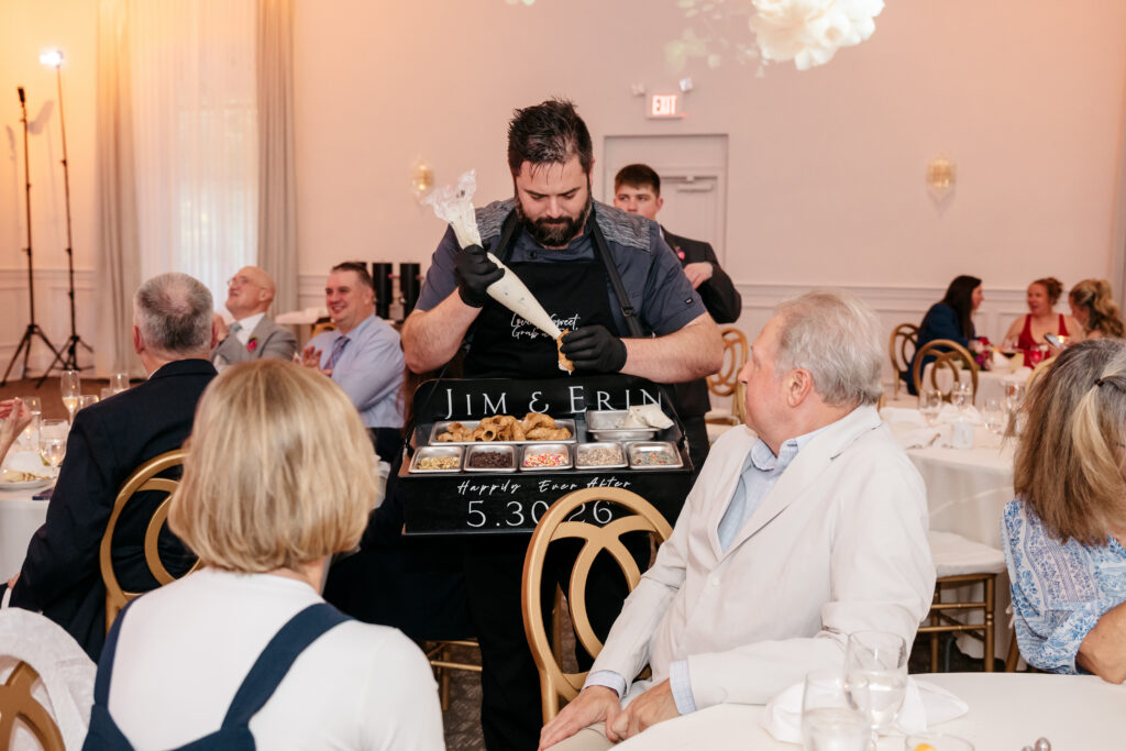 A man serves food from a tray at a wedding reception, with guests seated around decorated tables.