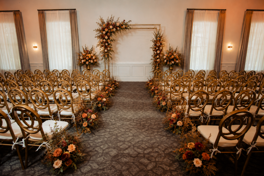 Wedding ceremony venue with gold chairs, floral aisle arrangements, and a flower-covered arch at the front.